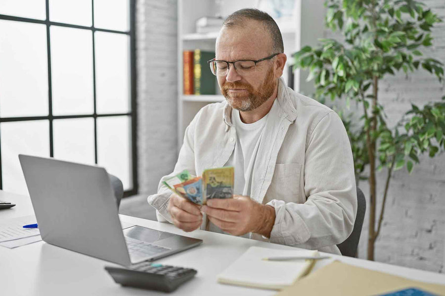 a man sitting at his laptop with Australian cash in his hands