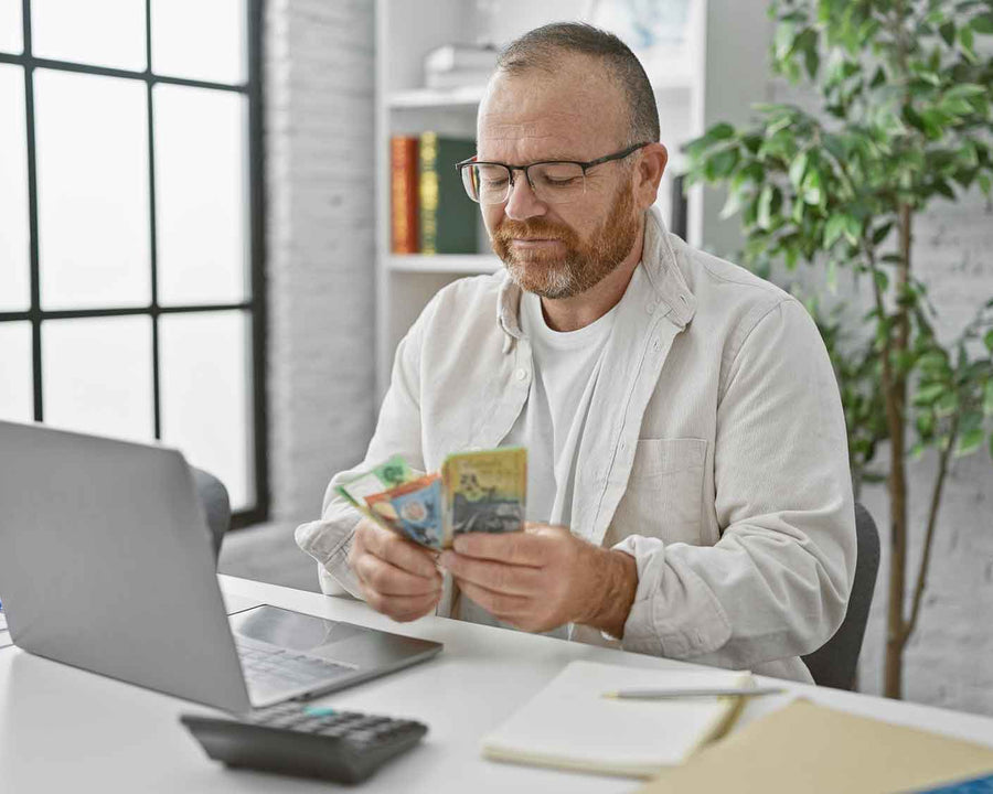 a man sitting at his laptop with Australian cash in his hands