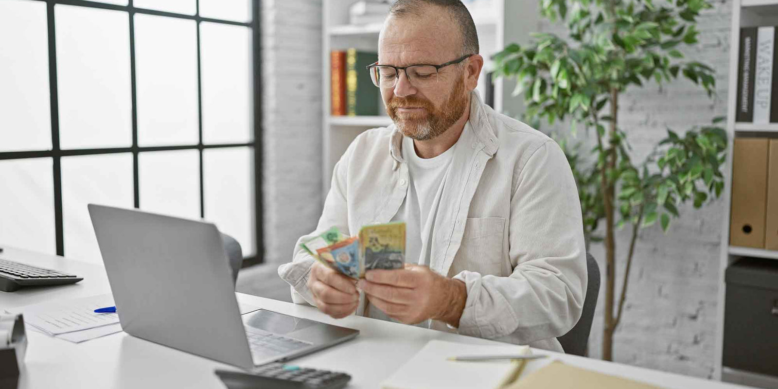 a man sitting at his laptop with Australian cash in his hands