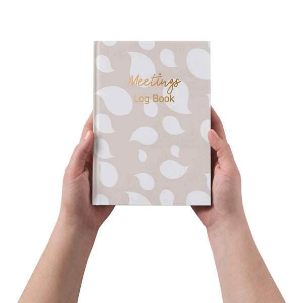 Hand holding a 'Meetings Log Book' with a patterned cover on a white background